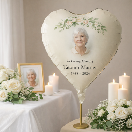 Heart-shaped balloon with a photo of an elderly woman and memorial text, surrounded by flowers and candles on a table.