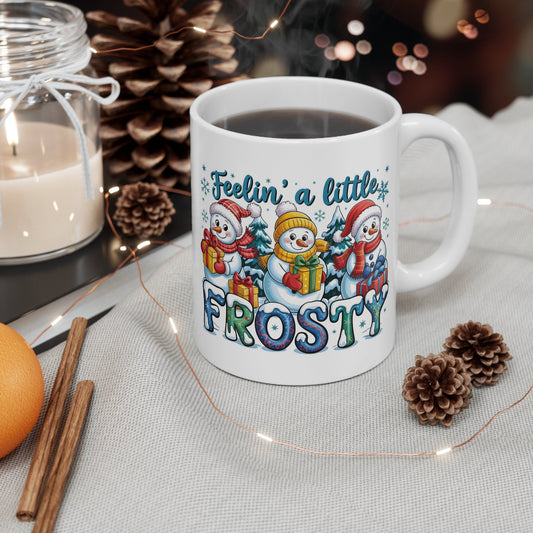 Feelin’ A Little Frosty snowman Christmas mug placed on a festive table with pinecones and holiday lights.