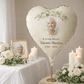 Personalised Heart-shaped balloon with a photo of an elderly woman and memorial text, surrounded by flowers and candles on a table.